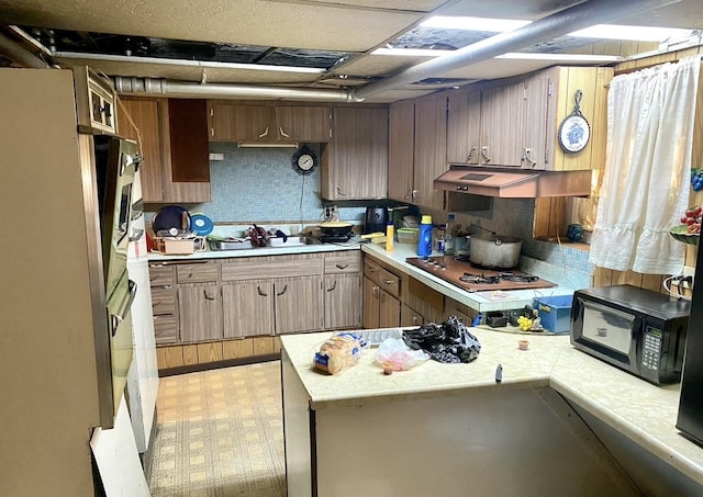4943 W Monroe St, Chicago, IL 60644 - kitchen with light countertops, under cabinet range hood, decorative backsplash, light flooring, and white gas cooktop