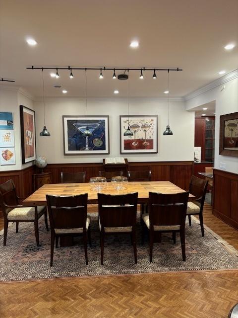 dining space with rail lighting, ornamental molding, and a wainscoted wall