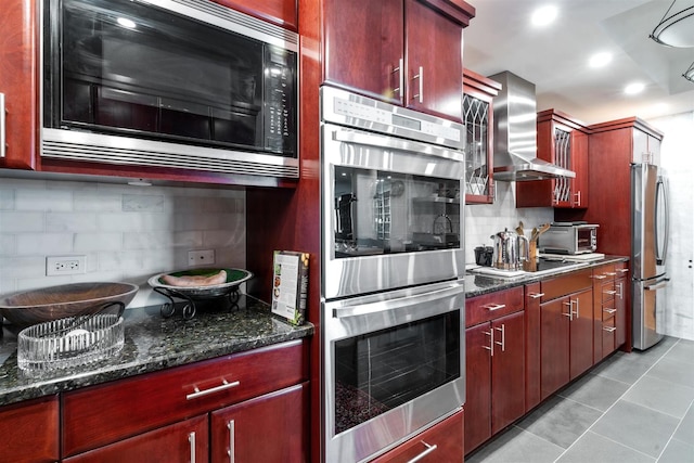kitchen featuring appliances with stainless steel finishes, wall chimney range hood, decorative backsplash, reddish brown cabinets, and light tile patterned flooring