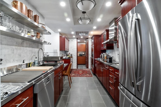 kitchen featuring appliances with stainless steel finishes, dark brown cabinets, a sink, wall chimney range hood, and decorative backsplash