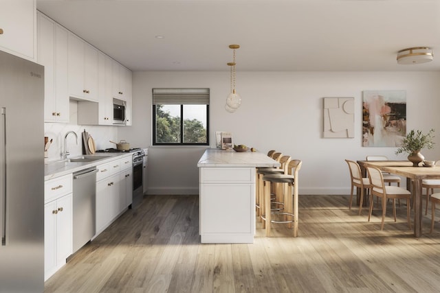 kitchen with stainless steel appliances, a sink, a kitchen breakfast bar, light countertops, and light wood-style flooring