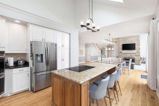 3211 Treyburn Rd, Naperville, IL 60564 - kitchen featuring stainless steel fridge with ice dispenser, a chandelier, black electric cooktop, light wood-style flooring, and a stone fireplace