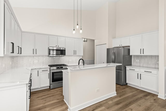 1468 W Grand Haven Rd, Romeoville, IL 60446 - kitchen featuring appliances with stainless steel finishes, a towering ceiling, tasteful backsplash, light wood-type flooring, and a center island with sink