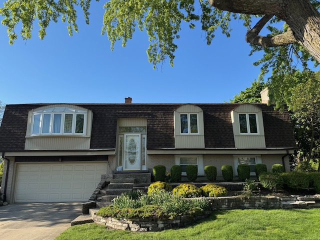 raised ranch featuring mansard roof, roof with shingles, a chimney, concrete driveway, and a garage