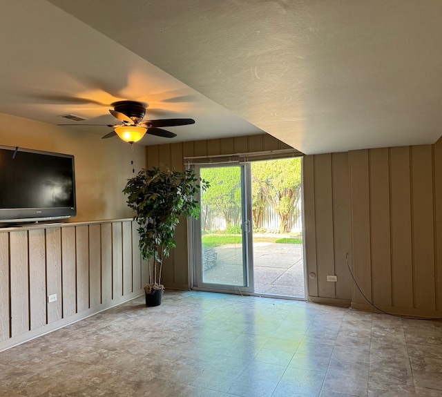 unfurnished living room featuring ceiling fan and wood walls