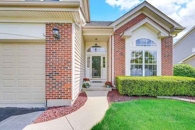 doorway to property with brick siding, a garage, asphalt driveway, and a yard