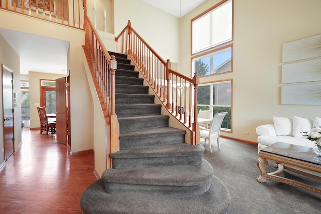 stairway featuring healthy amount of natural light, baseboards, a high ceiling, and wood finished floors