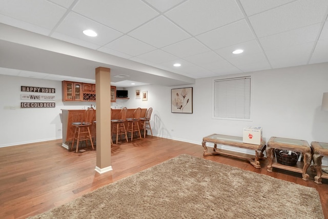 living area with bar, wood finished floors, baseboards, a drop ceiling, and recessed lighting