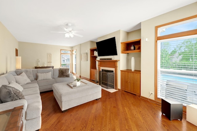 living area with a fireplace, ceiling fan, light wood-type flooring, and baseboards