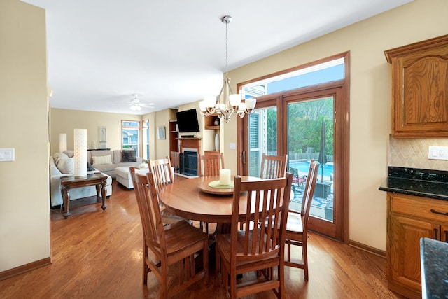 dining space with light wood-style flooring, a chandelier, baseboards, a fireplace, and a ceiling fan