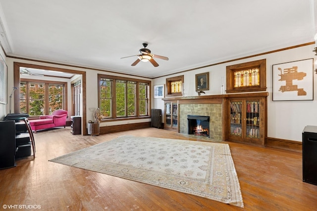 living area featuring ceiling fan, crown molding, wood finished floors, a tile fireplace, and baseboards
