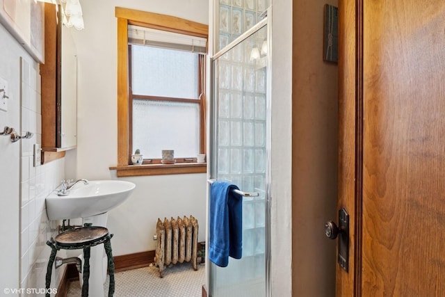bathroom featuring radiator, a shower stall, and baseboards