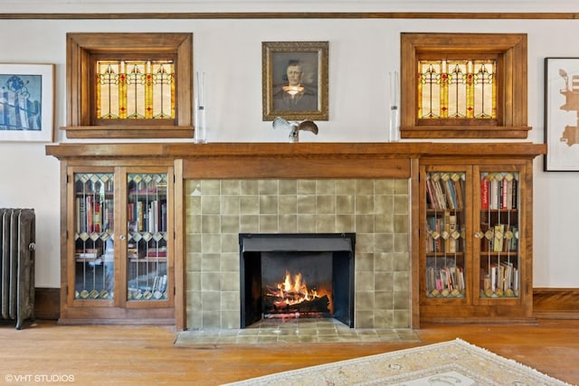 detailed view of radiator heating unit, wood finished floors, and a tiled fireplace