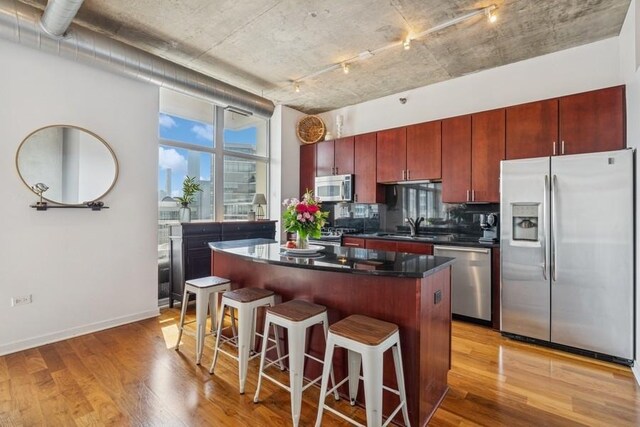kitchen featuring appliances with stainless steel finishes, a sink, rail lighting, a center island, and light wood-style flooring