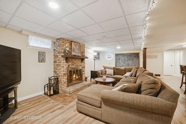 238 1st St, Cary, IL 60013 - living area featuring a brick fireplace, light wood finished floors, a paneled ceiling, baseboards, and rail lighting