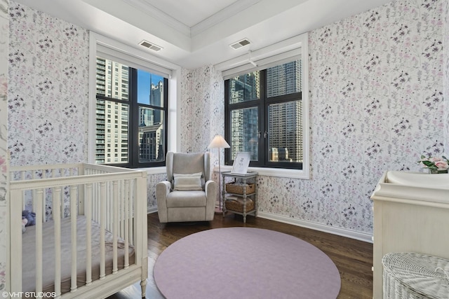 bedroom featuring wallpapered walls, crown molding, wood finished floors, a crib, and baseboards