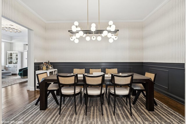 dining space featuring a chandelier, ornamental molding, wood finished floors, wainscoting, and wallpapered walls