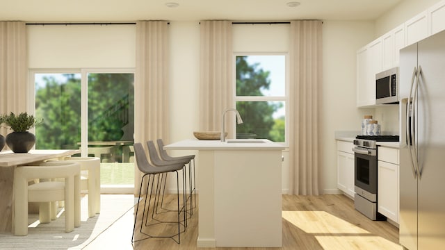 kitchen with stainless steel appliances, a sink, light wood-style flooring, light countertops, and an island with sink