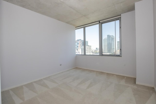 unfurnished room featuring light carpet, a city view, and baseboards