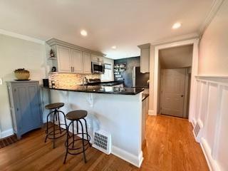 1010 N Patton Ave, Arlington Heights, IL 60004 - kitchen with stainless steel microwave, a peninsula, ornamental molding, a kitchen breakfast bar, and wood finished floors