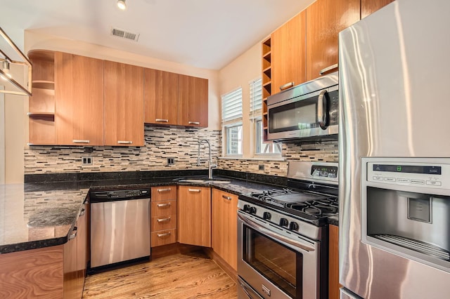 kitchen with appliances with stainless steel finishes, open shelves, a sink, and tasteful backsplash