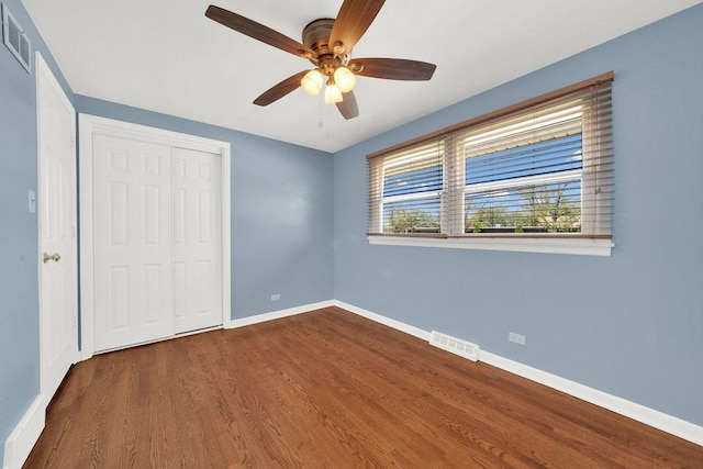 unfurnished bedroom with dark wood-style flooring, a closet, baseboards, and a ceiling fan