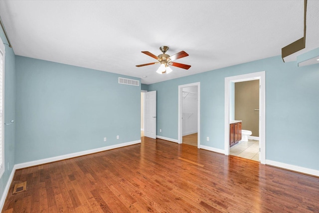 1208 Waters Edge Rd, Champaign, IL 61822 - unfurnished bedroom with a walk in closet, a closet, wood finished floors, a ceiling fan, and connected bathroom