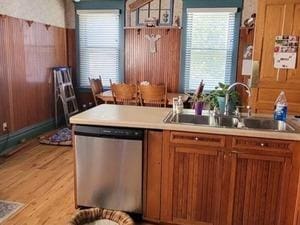 kitchen featuring dishwasher, a sink, brown cabinetry, light countertops, and light wood-style flooring