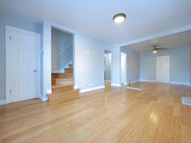 unfurnished living room featuring hardwood / wood-style flooring, stairs, ceiling fan, and baseboards