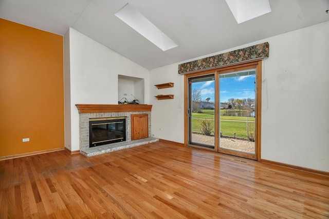 unfurnished living room featuring a skylight, lofted ceiling, light wood finished floors, a fireplace, and baseboards