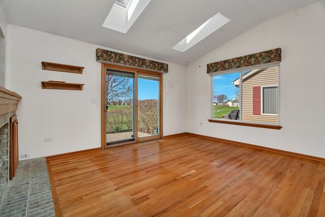 unfurnished room with a skylight, vaulted ceiling, wood finished floors, a brick fireplace, and baseboards