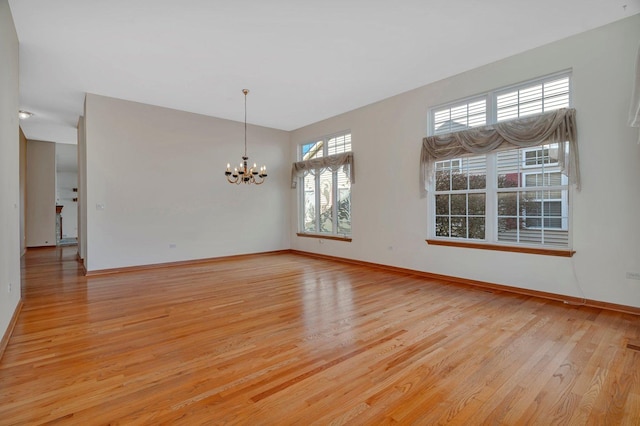 empty room featuring a chandelier, light wood finished floors, and baseboards