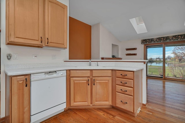 kitchen featuring white dishwasher, a skylight, a sink, lofted ceiling, and a peninsula