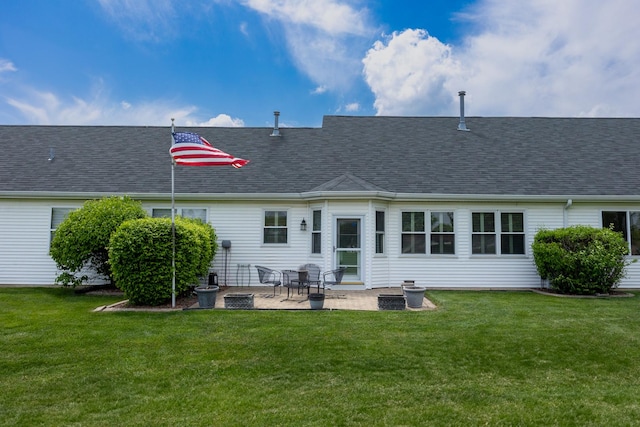 back of house with roof with shingles, a lawn, and a patio area