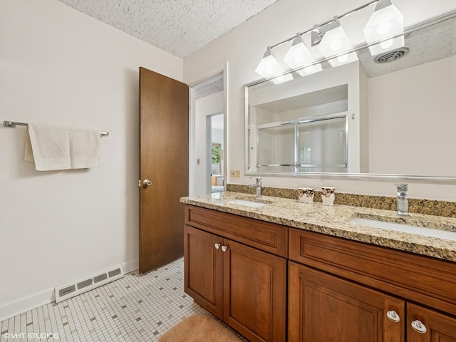 bathroom with a shower stall, double vanity, a textured ceiling, and baseboards