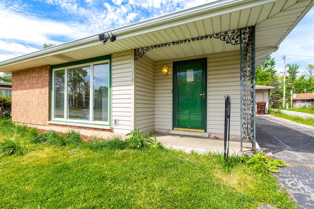 property entrance featuring brick siding, a yard, covered porch, and asphalt driveway