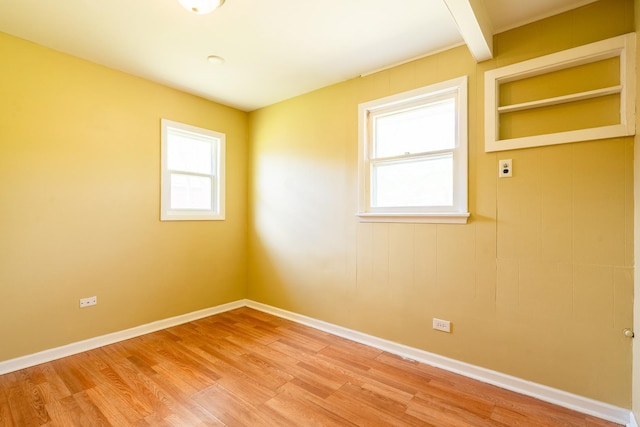 spare room featuring light wood finished floors, baseboards, and beam ceiling