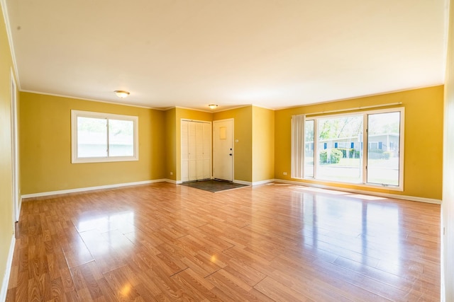 unfurnished room with healthy amount of natural light, wood finished floors, baseboards, and ornamental molding