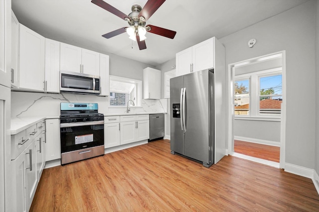 kitchen featuring stainless steel appliances, a ceiling fan, white cabinets, and light wood-type flooring