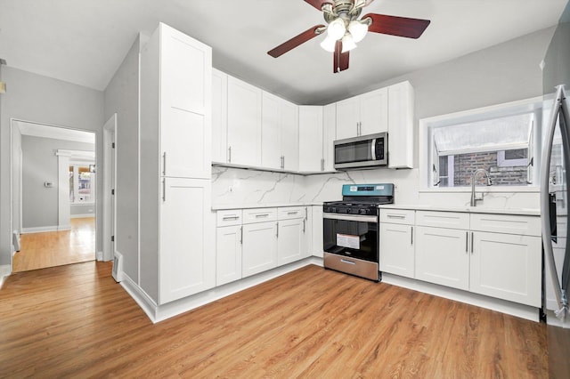 kitchen with stainless steel appliances, light countertops, a ceiling fan, light wood-type flooring, and white cabinets