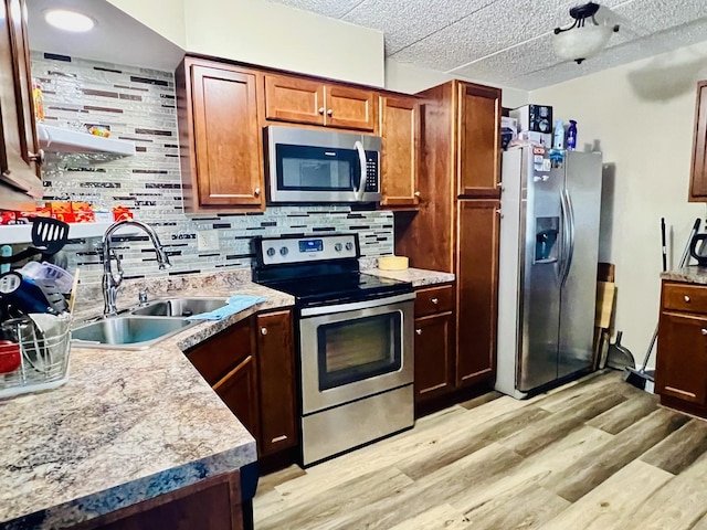 kitchen featuring stainless steel appliances, a sink, light wood-type flooring, and backsplash