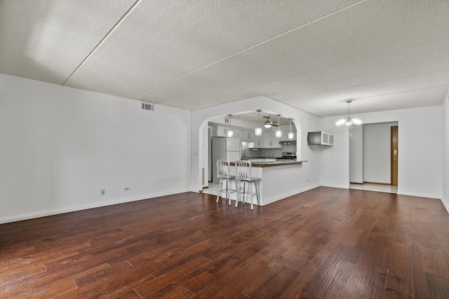 unfurnished living room featuring a chandelier, dark wood-type flooring, a textured ceiling, arched walkways, and baseboards