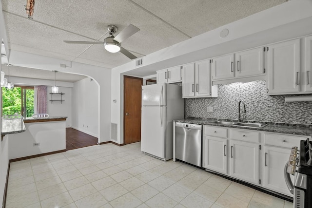kitchen featuring stainless steel appliances, a sink, a ceiling fan, arched walkways, and dark stone countertops