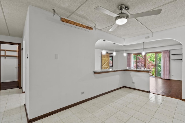 unfurnished room with arched walkways, ceiling fan, baseboards, light tile patterned floors, and a textured ceiling