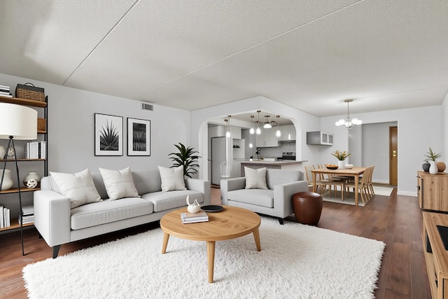 living room featuring arched walkways, a chandelier, dark wood finished floors, a textured ceiling, and baseboards