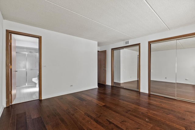 unfurnished bedroom featuring two closets, hardwood / wood-style floors, ensuite bathroom, and a textured ceiling