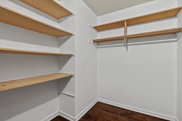walk in closet with built in desk and dark wood-style flooring