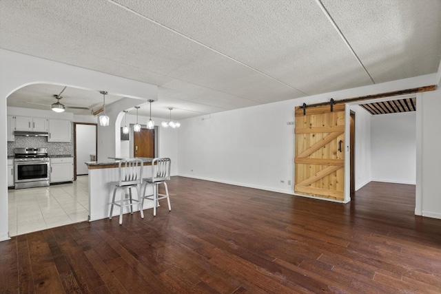 kitchen with stainless steel range, open floor plan, dark countertops, under cabinet range hood, and hardwood / wood-style floors