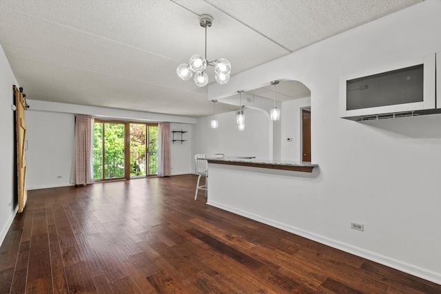 unfurnished living room with wood finished floors, baseboards, a textured ceiling, arched walkways, and a chandelier