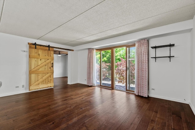 empty room with a barn door, wood finished floors, baseboards, and a textured ceiling
